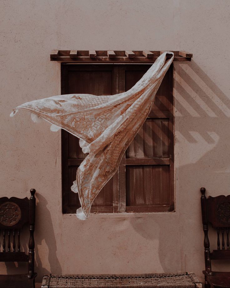 an old building with two wooden chairs and a sheer curtain hanging from it's window