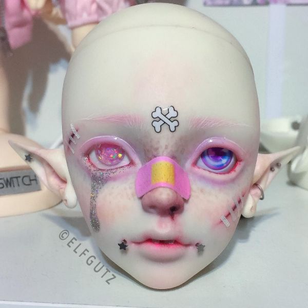 a close up of a doll's face with pink and yellow eyeliners