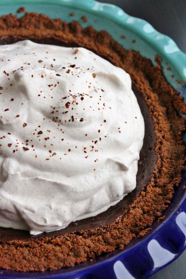 a chocolate pie with whipped cream on top in a blue and white bowl, ready to be eaten