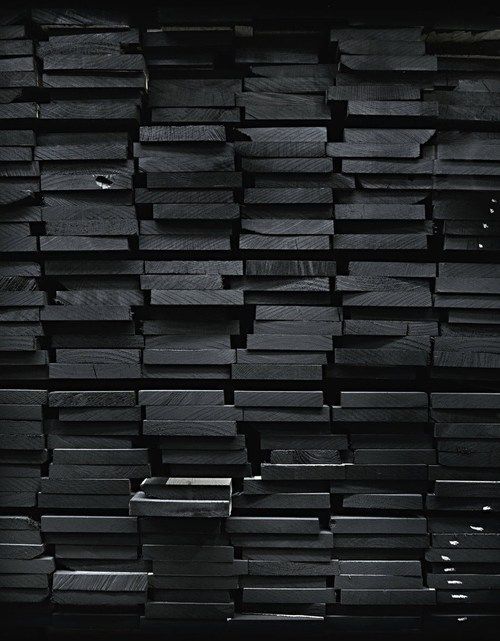 a large stack of black wooden planks stacked on top of each other in the dark