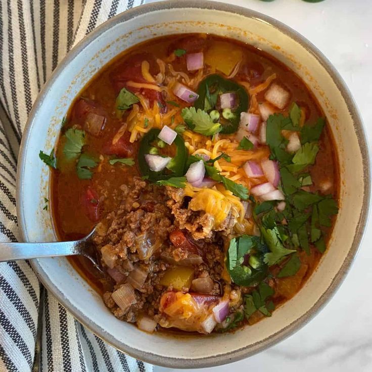 a bowl of chili soup with meat, cheese and cilantro on the side