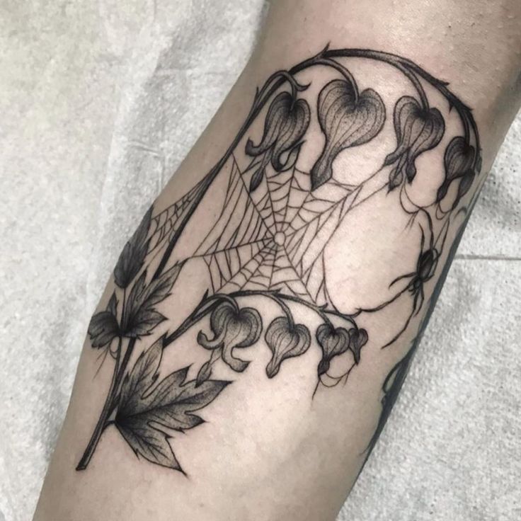 a black and white photo of a spider web tattoo on the left arm with leaves