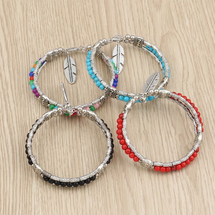 four bracelets with different colored beads on a wooden surface, one has an arrow and the other has a feather