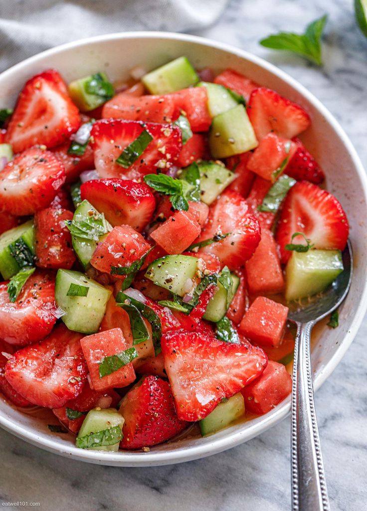 a white bowl filled with sliced strawberries and cucumber on top of a marble table