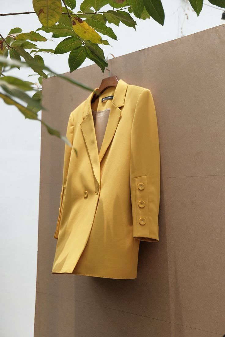 a yellow suit hanging on a wall next to a green leafy tree in front of it