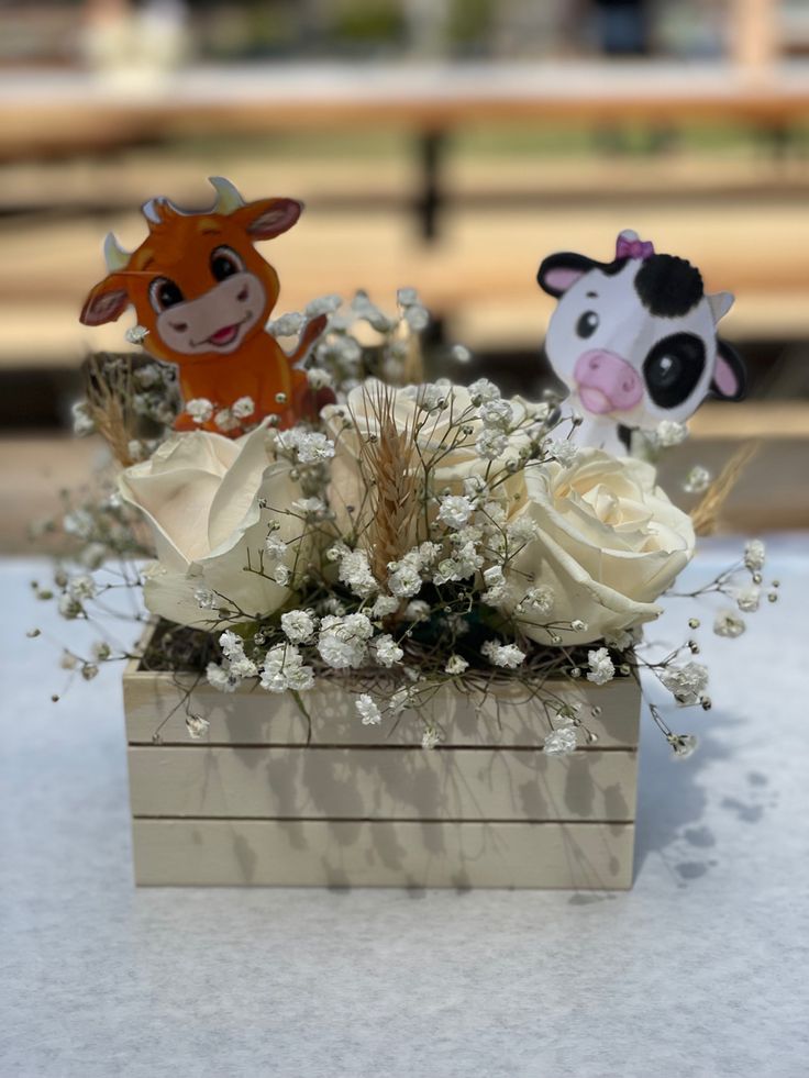 two small cow figurines sitting on top of a flower box filled with white flowers