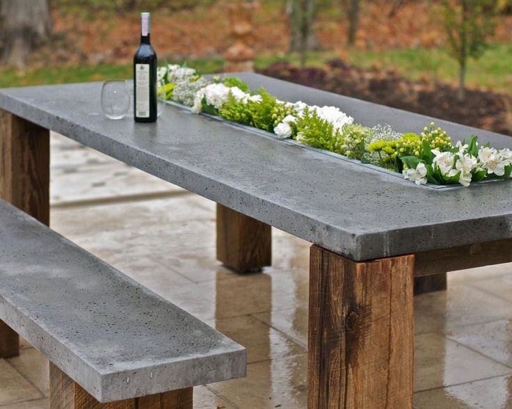 a concrete table with flowers and a bottle of wine sitting on top of it next to a bench