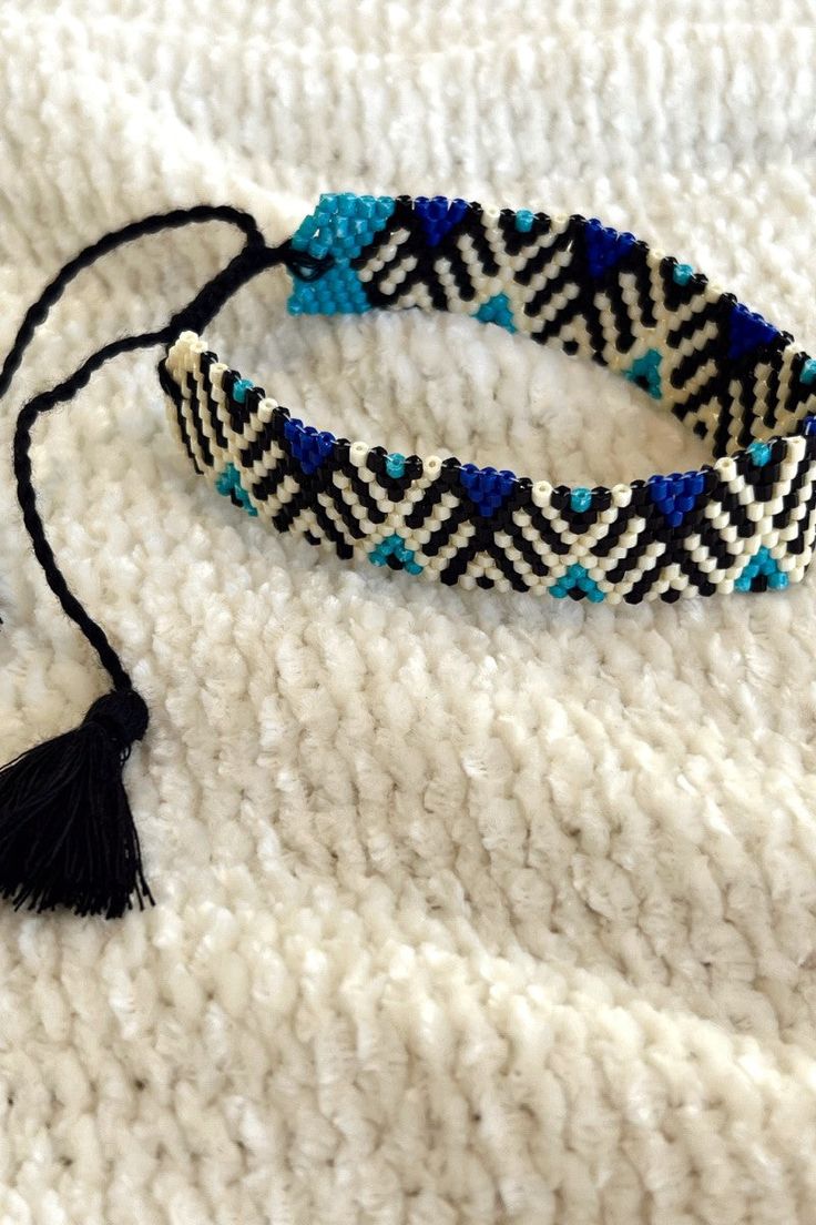 Close image of the Forever Yours Beaded Bracelet that features black, white, and blue beading with an adjustable black tasseled tie. Bohemian Black Friendship Bracelets With Sliding Knot, Black Bohemian Friendship Bracelets With Sliding Knot, Black Bohemian Resizable Friendship Bracelets, Black Woven Friendship Bracelets For Festival, Black Woven Beaded Bracelets For Festival, Adjustable Black Woven Friendship Bracelets, Handwoven Black Bracelet Jewelry, Adjustable Black Handwoven Beaded Bracelets, Bohemian Black Handwoven Beaded Bracelets