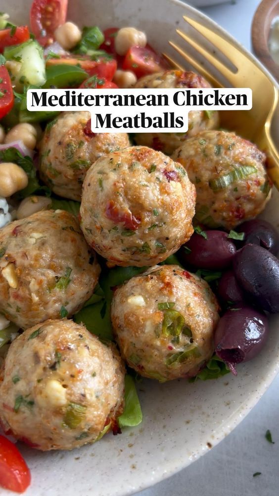 a white plate topped with meatballs next to a fork and salad on top of a table