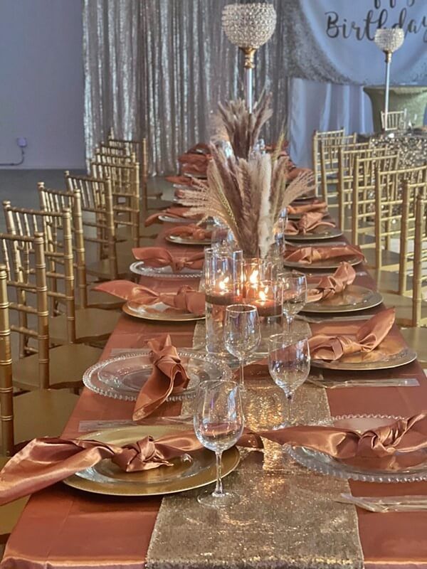 the table is set with gold plates, silverware and pink napkins on it