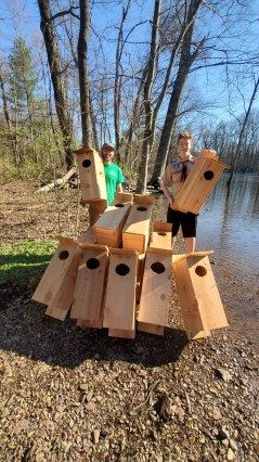 two young boys playing with wooden birdhouses in the woods next to a lake and trees