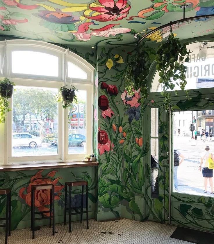 the interior of a restaurant with painted flowers on the walls and ceiling, along with two windows