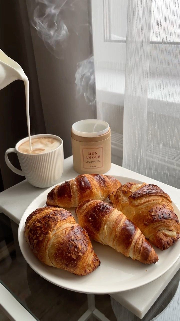 three croissants on a plate next to a cup of coffee