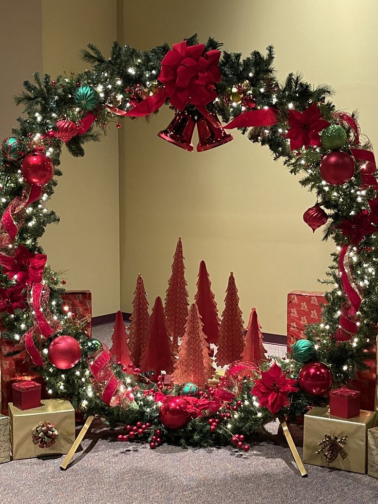 a christmas wreath with red and green ornaments on it, surrounded by presents under the tree