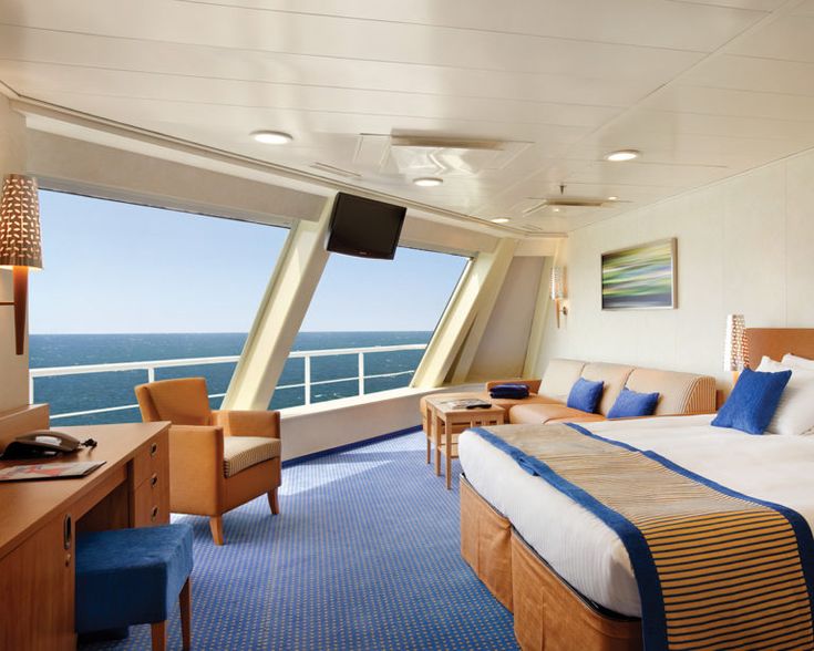 a bedroom with a bed, desk and television on the ship's balcony overlooking the ocean