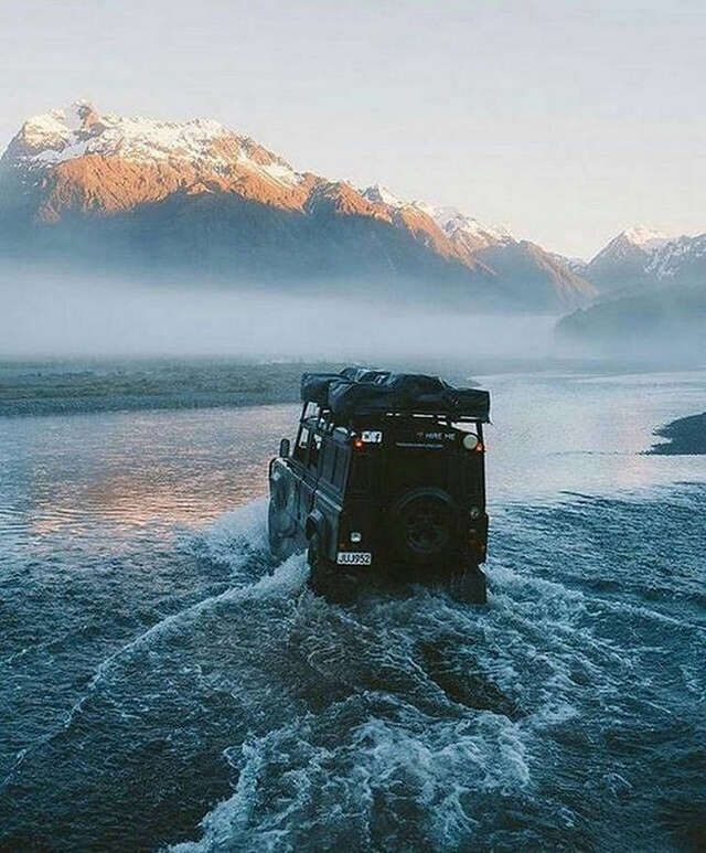 a jeep driving through the water with mountains in the background and hearts shaped above it