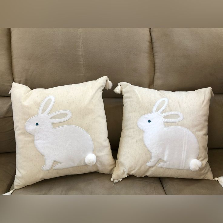 two pillows with white rabbits on them sitting on a couch