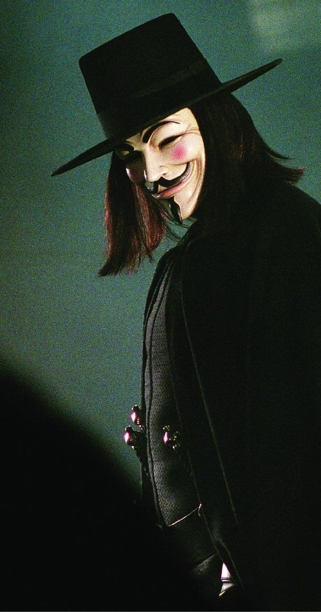 a man in a black hat and coat with long hair wearing a mask on his face