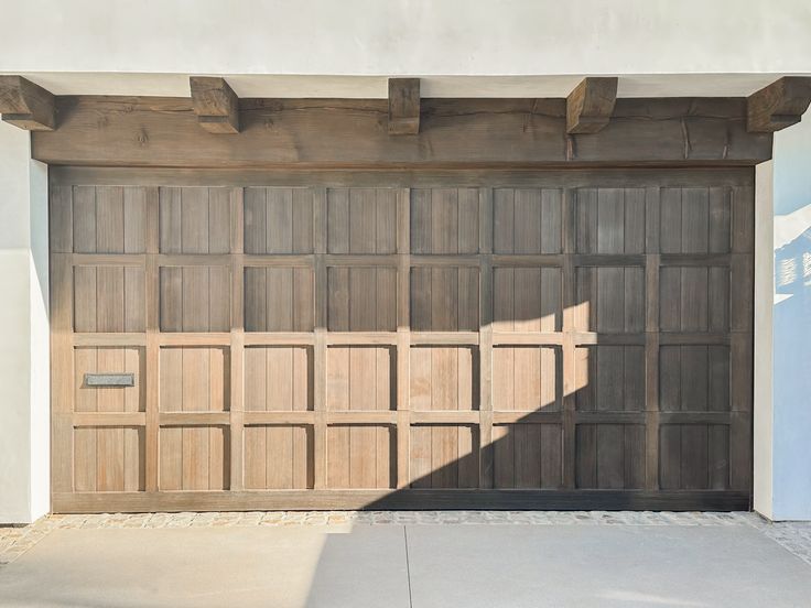 a wooden garage door in front of a white building with a shadow on the ground