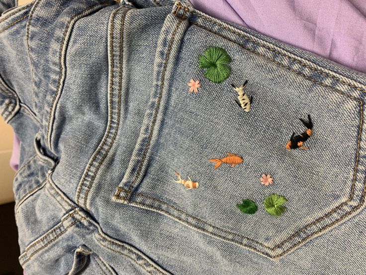 there are 4 embroidered koi fish all different variations of black white and orange. there are three lily pads surrounding them and two lily flowers. it’s all on the back pocket of a jeans Embroidered Jeans Diy, Koi Fish Shirt, Embroidery Jeans Diy, Jeans Pocket, Clothes Embroidery Diy, Denim Embroidery, Basic Embroidery Stitches, Diy Embroidery Patterns, Embroidery On Clothes