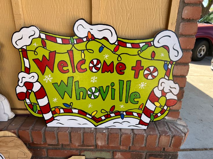 a welcome sign on the side of a brick wall next to a teddy bear and christmas decorations