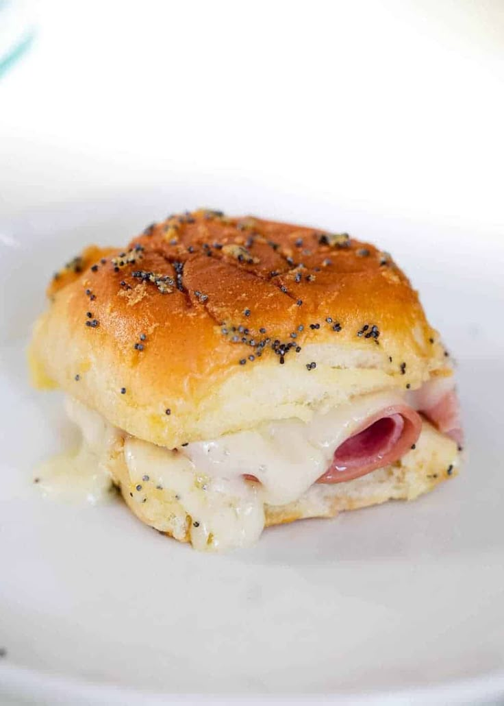 a ham and cheese slider on a white plate with black sprinkles