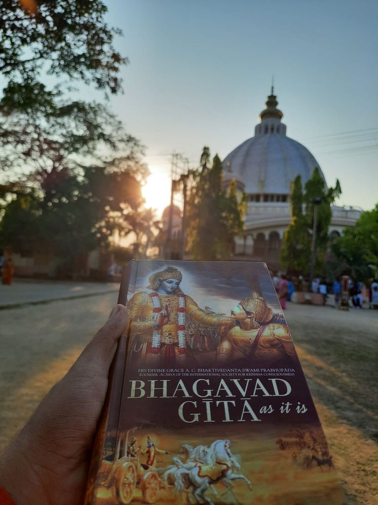 a person holding up a book in front of a building with a dome on top