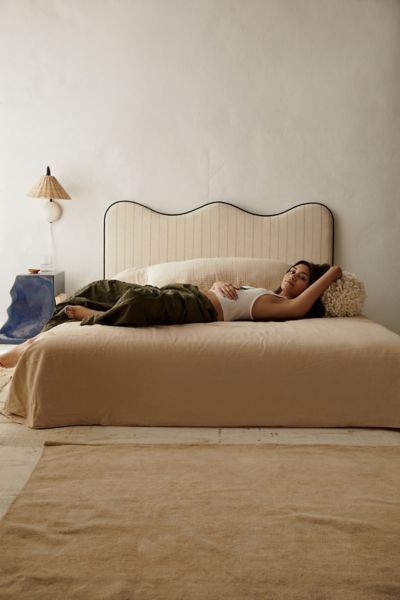 a woman laying on top of a bed next to a lamp and floor rug in a room