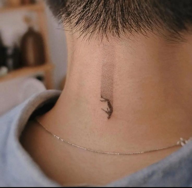 a person with a small bird tattoo on their neck and behind the neck is a chain