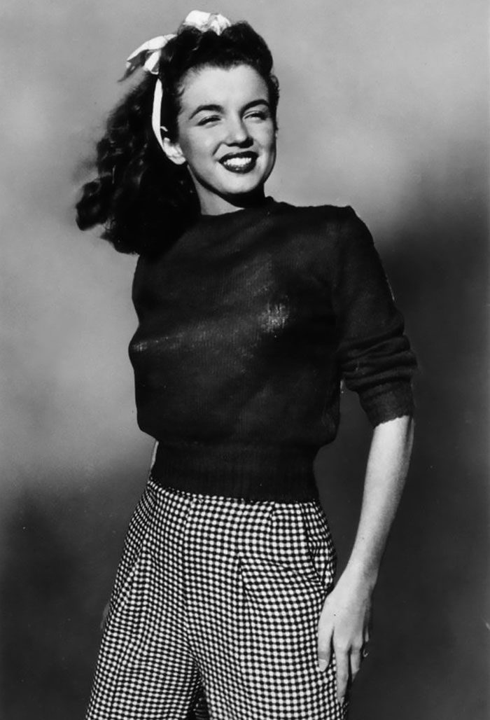 a black and white photo of a woman with her hair in a ponytail wearing plaid pants