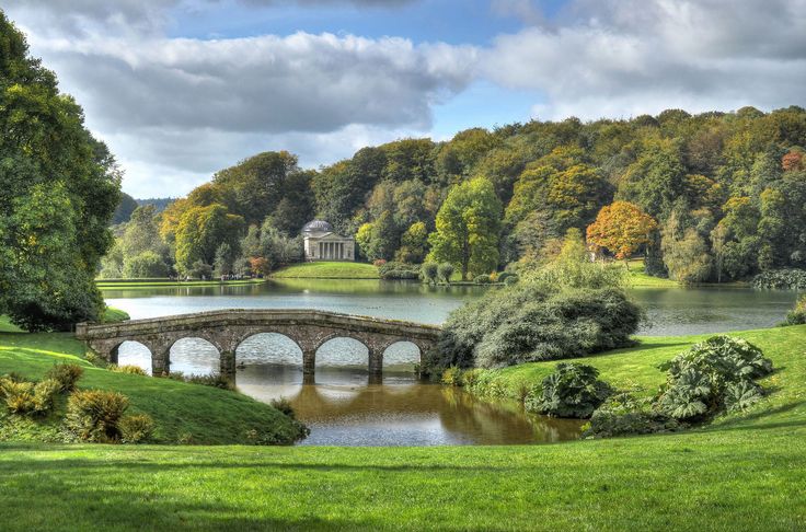 a painting of a bridge over a lake in the middle of a lush green park