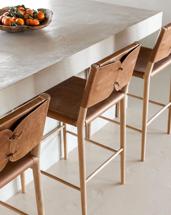 a bowl of oranges sitting on top of a table next to four wooden chairs