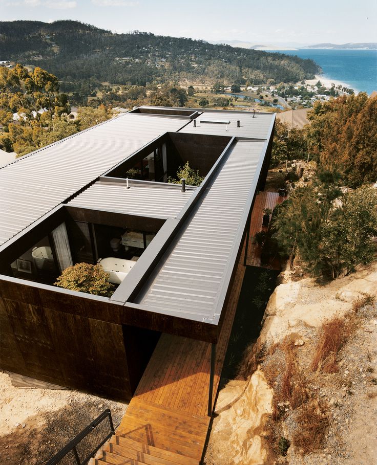 an aerial view of a modern house on top of a cliff overlooking the ocean and mountains