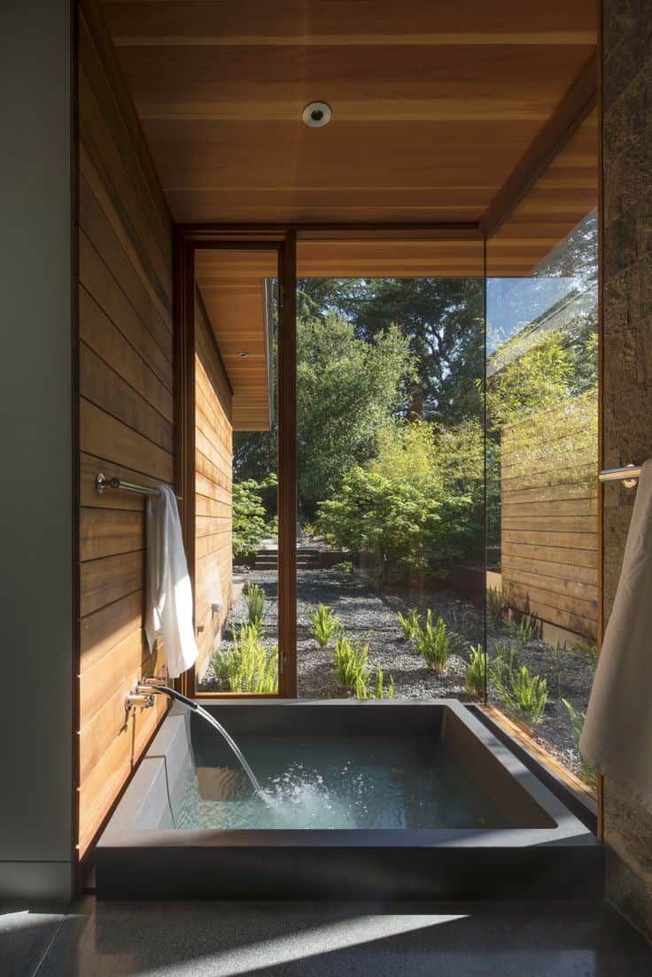 an outdoor jacuzzi tub in the middle of a room with wooden walls and windows