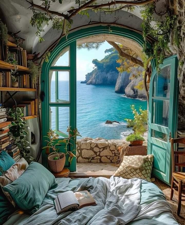 a bedroom with an open window overlooking the ocean and cliffs in the distance is shown