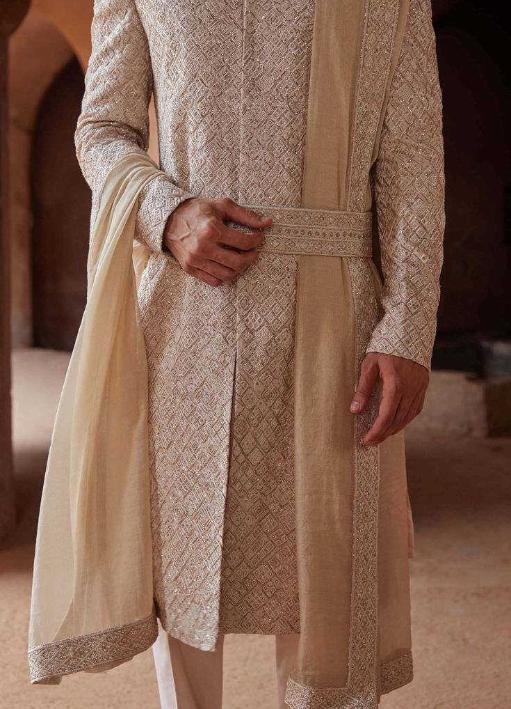 Editor's Note Step into elegance with our mushroom raw silk sherwani, adorned with intricate tonal resham embroidery and delicate rose gold pitta work all over. Paired with a monga tussar kurta and cotton lycra trousers, this ensemble effortlessly blends modern aesthetics with classic charm. Perfect for showcasing a refined and sophisticated look on your special occasion. Note: Stole and belt are for styling purposes only. Fabric: Raw silk, monga tussar and cotton Color: Beige Components: Sherwa Raw Silk Bandhgala For Reception At Eid, Eid Bandhgala In Raw Silk For Reception, Eid Reception Bandhgala In Raw Silk, Raw Silk Unstitched Suit With Naqshi For Wedding, Wedding Unstitched Suit In Raw Silk With Naqshi, Silk Unstitched Suit With Naqshi For Wedding, Traditional Silk Churidar For Reception, Cream Churidar For Reception In Transitional Season, Cream Churidar For Reception