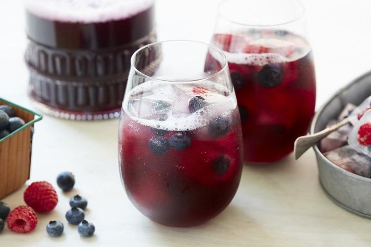 two glasses filled with blueberries and raspberries next to a tin of ice