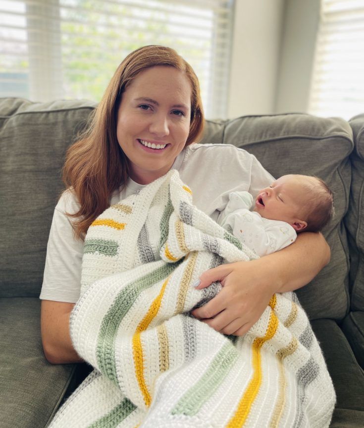 a woman sitting on a couch holding a baby wrapped up in a blanket and smiling at the camera