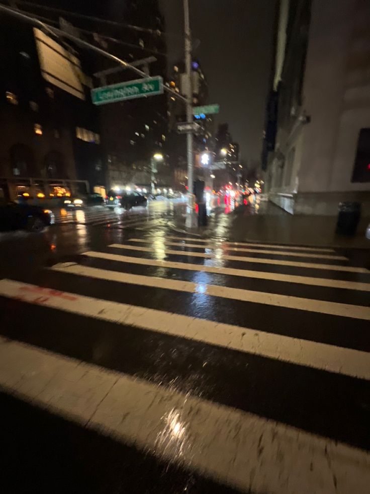 a city street at night with traffic lights and people crossing the street in the rain