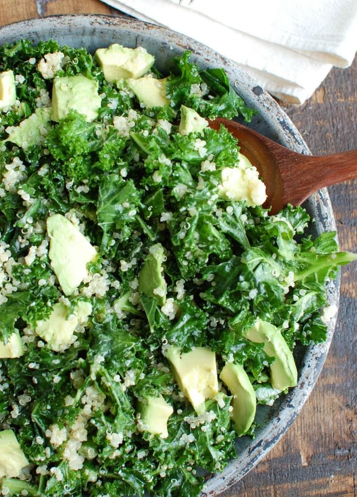 a bowl filled with greens and avocado on top of a wooden table next to a napkin