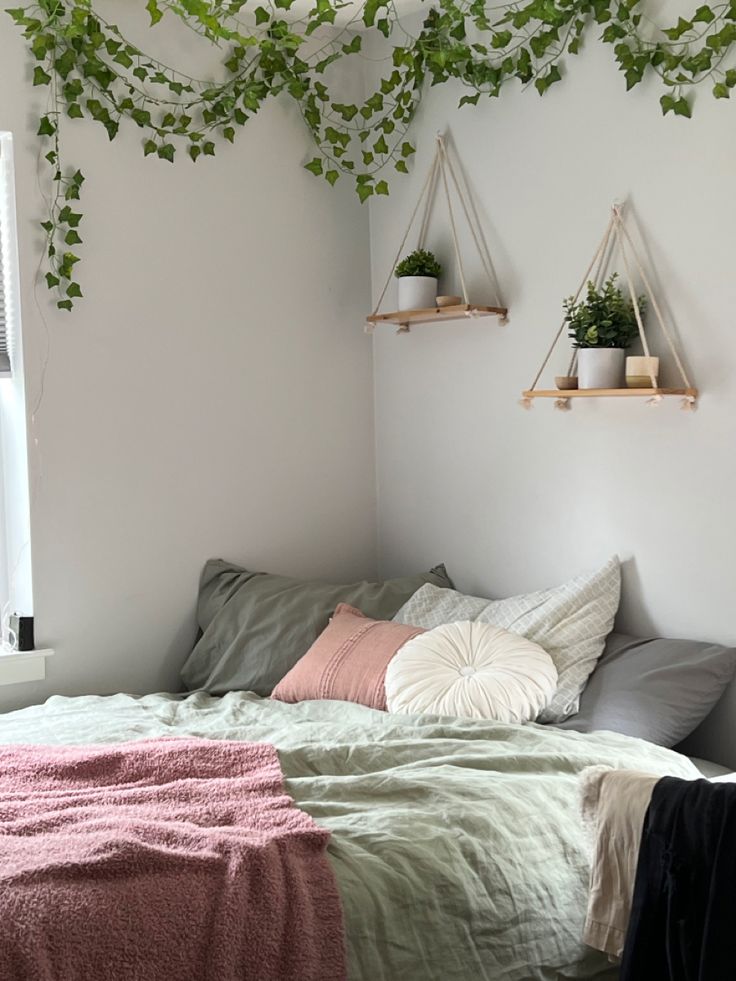 an unmade bed with green plants hanging from the ceiling and pillows on top of it