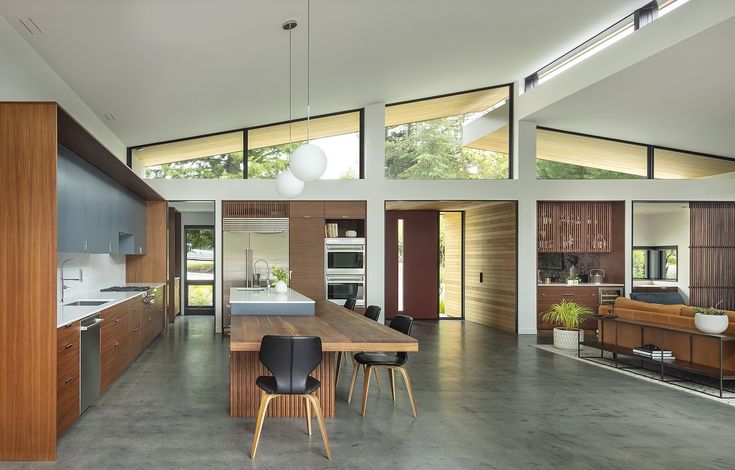 an open kitchen and dining area with wooden cabinets, counter tops, and floor to ceiling windows