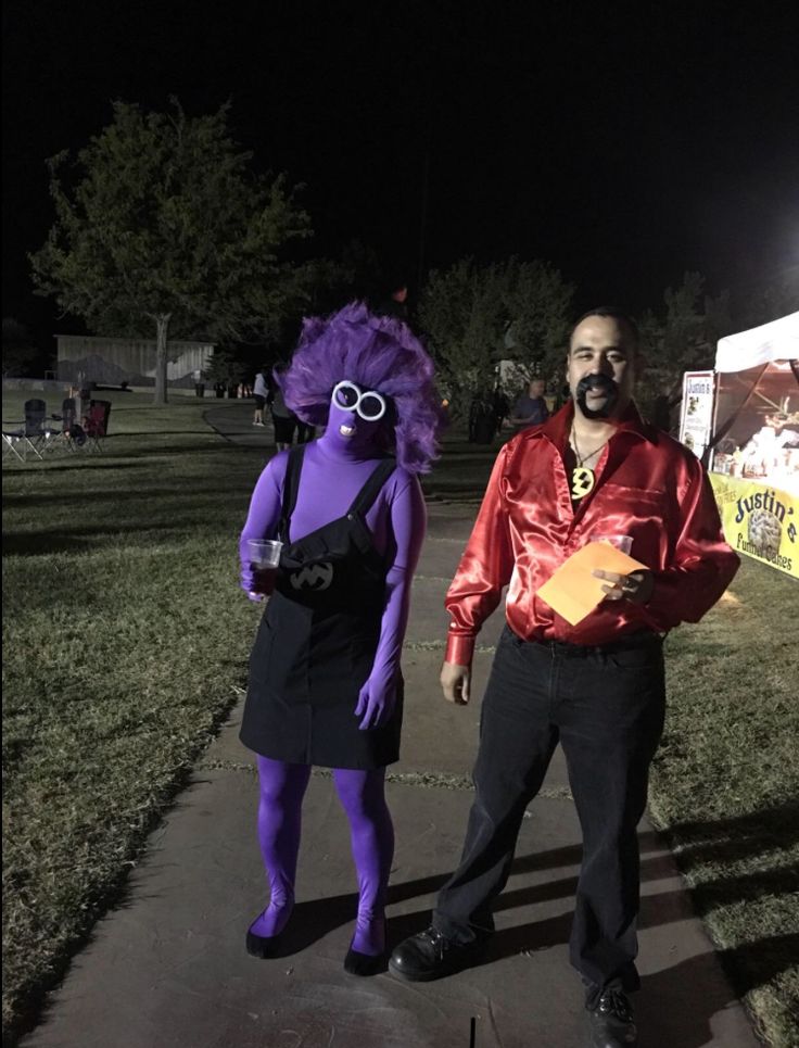 a man and woman in costume standing next to each other on a sidewalk at night