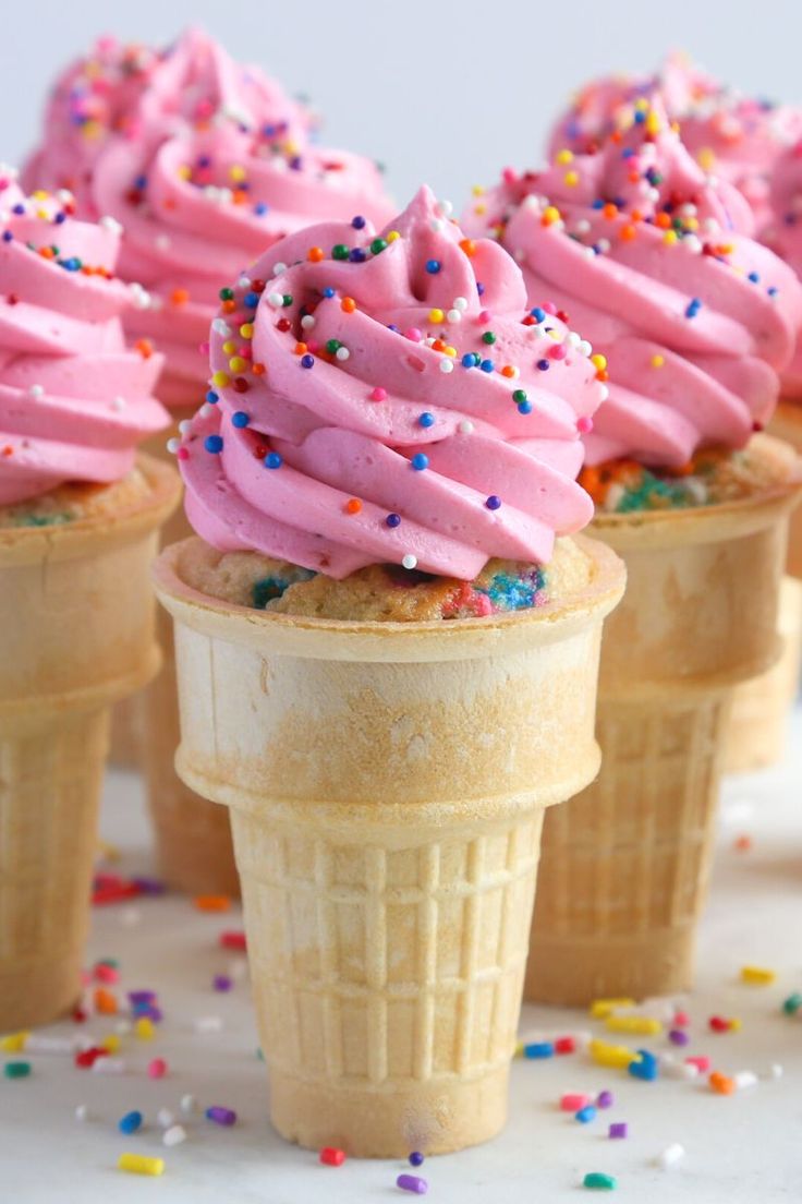 three ice cream cones with pink frosting and sprinkles on white surface