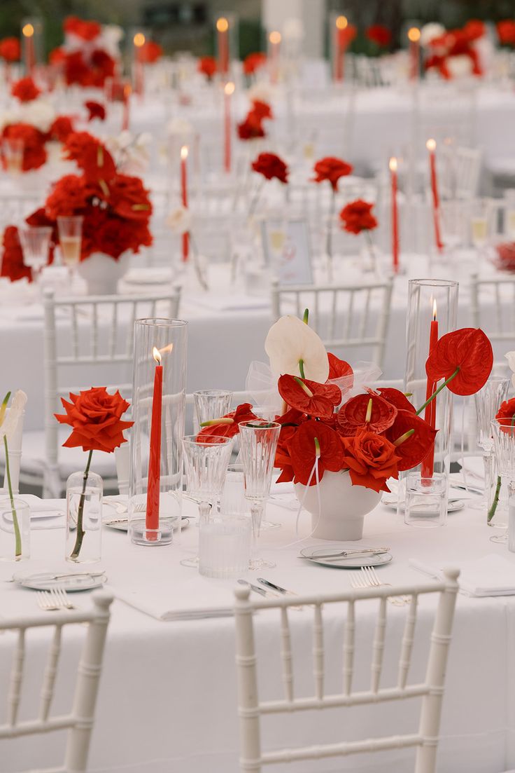 the tables are set with white linens and red flowers in vases on them