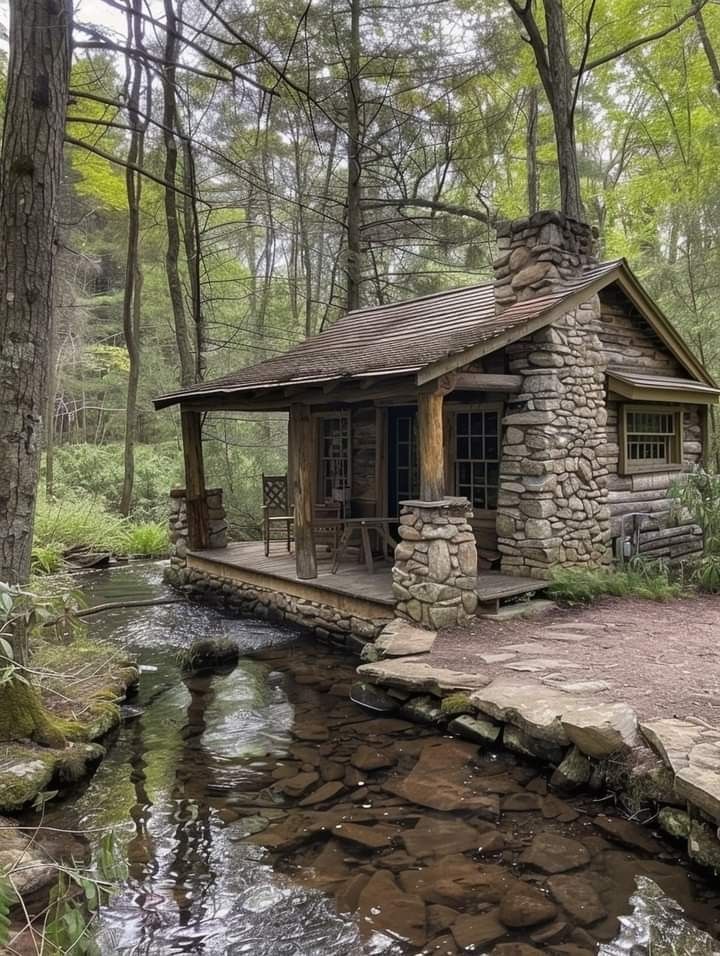 a small cabin in the woods next to a stream with rocks and water running through it