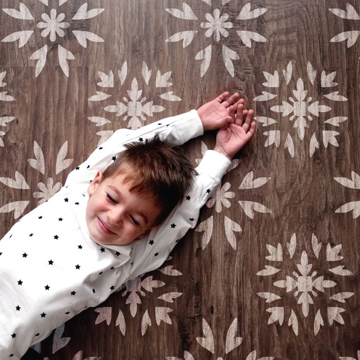 a little boy laying on top of a wooden floor next to a flowery wallpaper