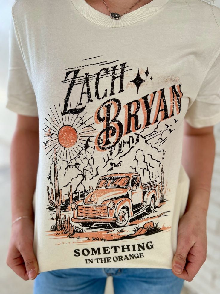 "Get ready to hit the road with the PLUS Zach Bryan Truck Tee! Featuring lyrics from his hit song "Something in the Orange", this cream graphic tee will add a touch of western charm to any outfit. Its short sleeves and crew neck make it perfect for any adventure. Yeehaw!" Cream Graphic Tee, Something In The Orange, Small Business Signs, Zach Bryan, Hit The Road, Glitz And Glam, Hit Songs, The Road, Graphic Tee