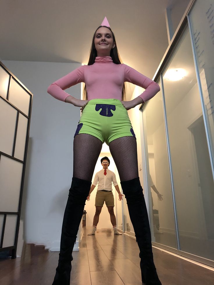 a woman in green and pink outfit standing next to a man wearing white shirt and black boots