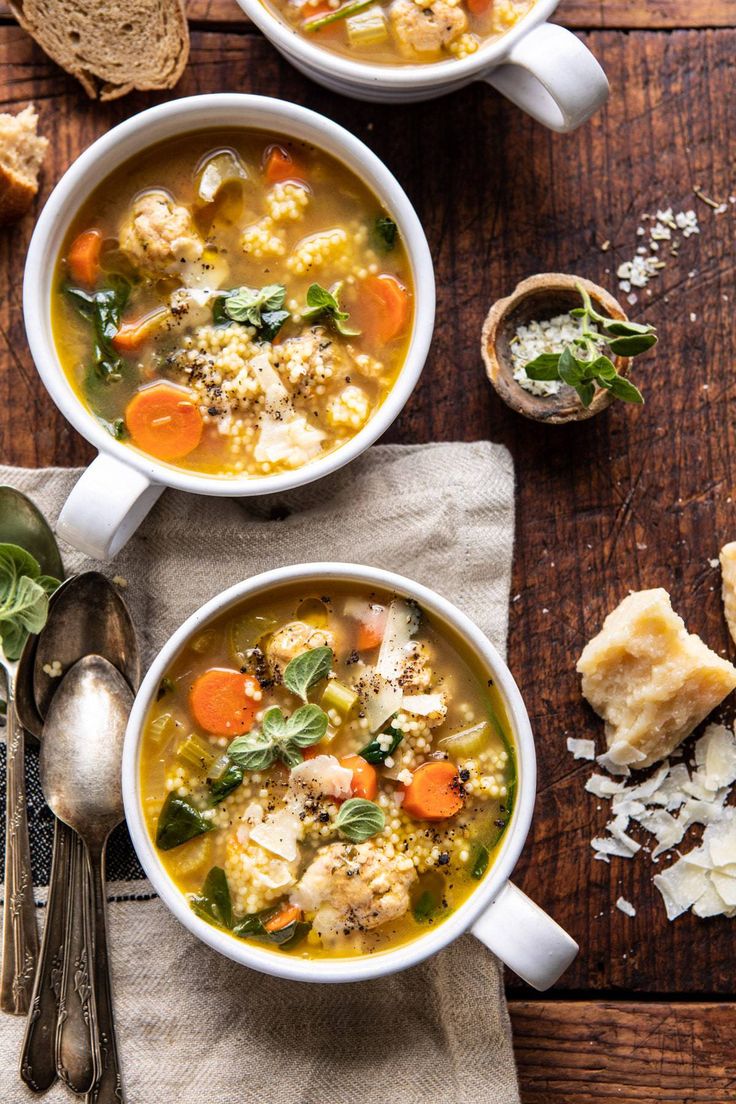 two bowls of soup on a wooden table with bread and spoons next to it